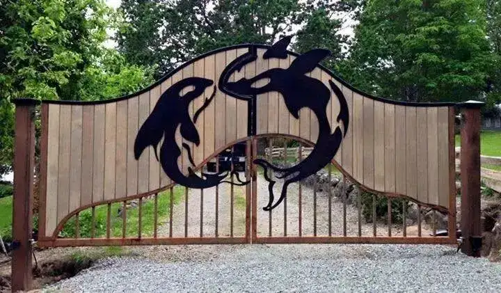 Arched cedar driveway gate with two steel orcas